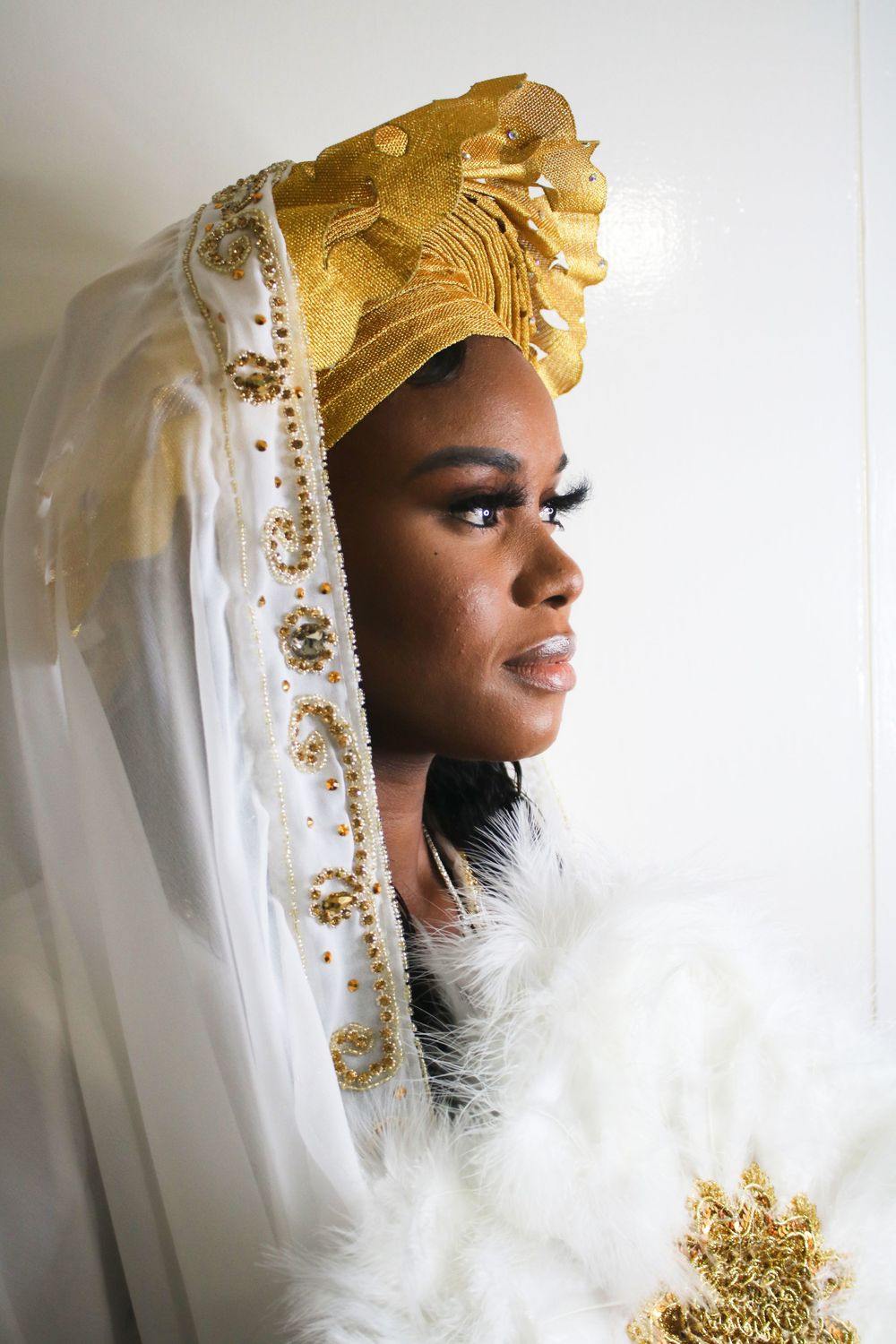 Profile portrait with ornate gold and white headpiece and feather details.