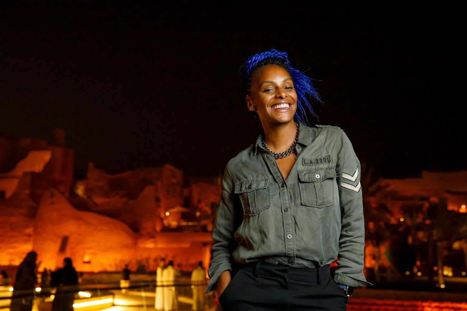 Person in casual attire smiling at night with desert landscape in background.