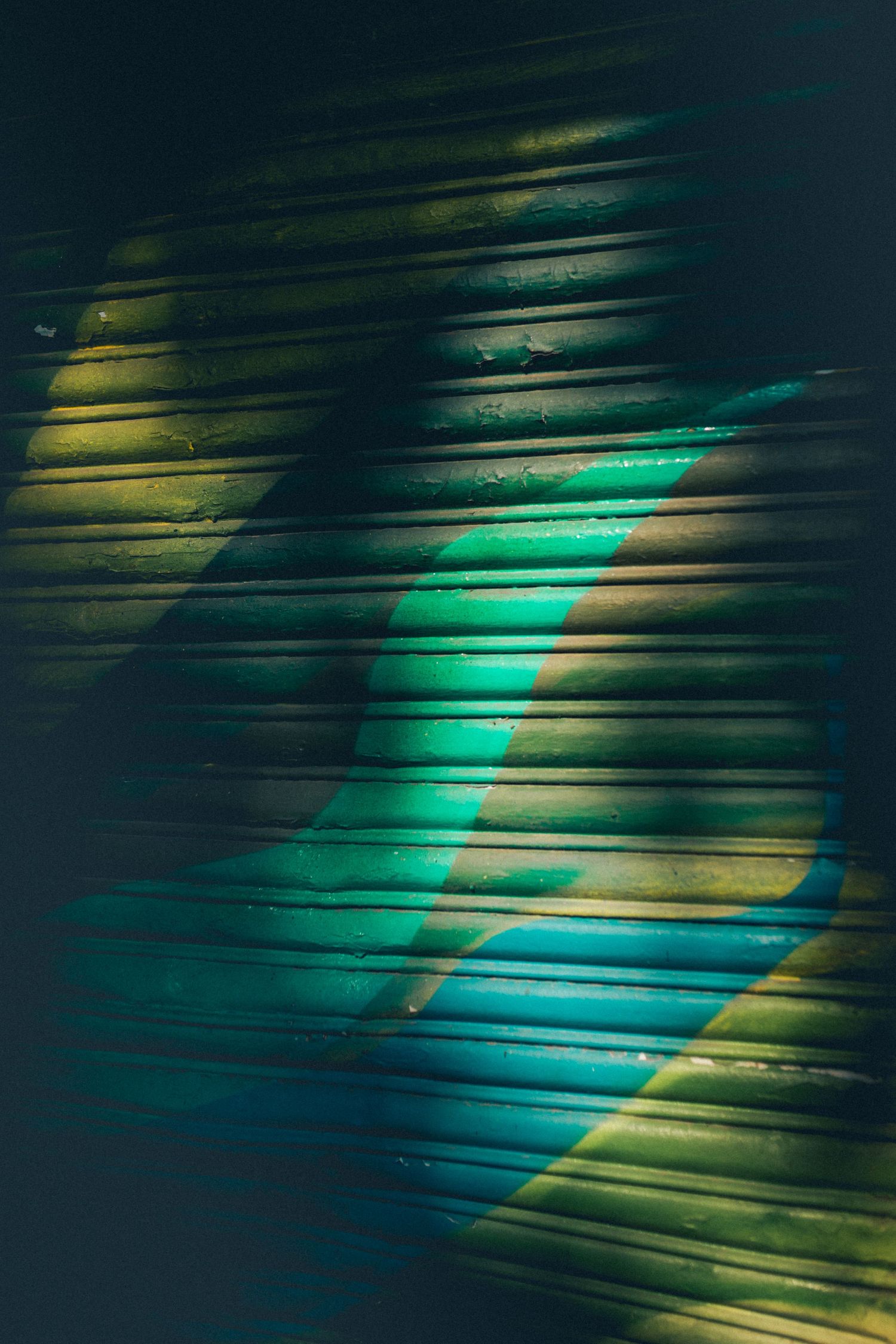 Abstract pattern of turquoise and yellow light streaming through window blinds.