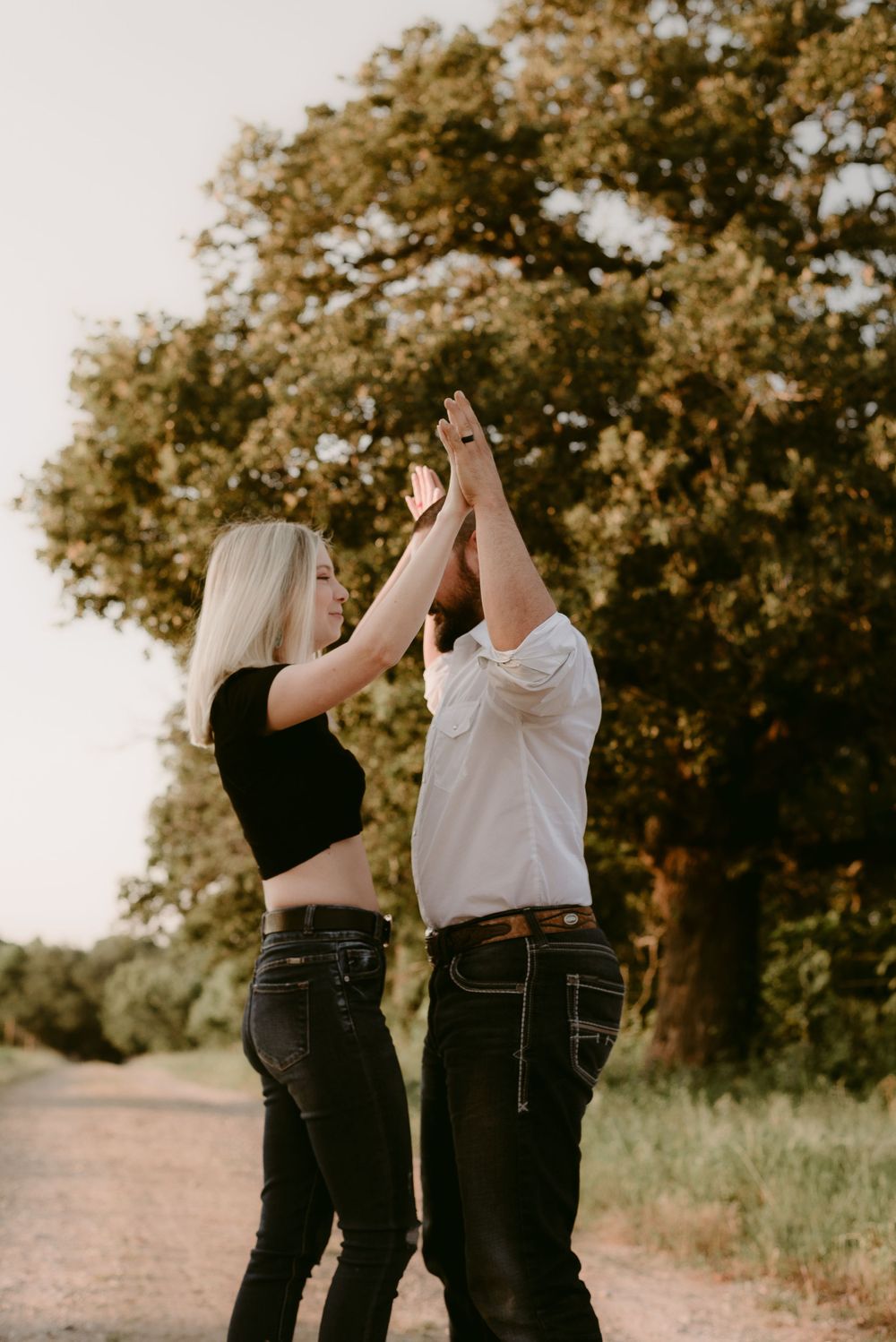 A couple holds hands high together in a playful pose on a countryside path.