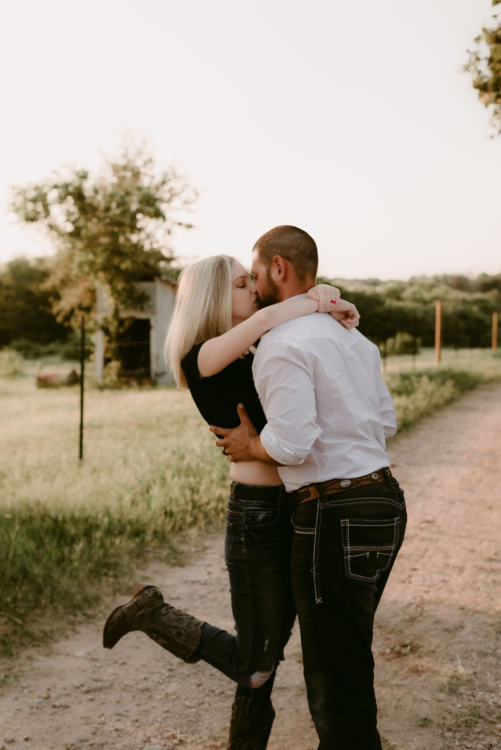 A couple shares a romantic embrace on a rural path during golden hour.