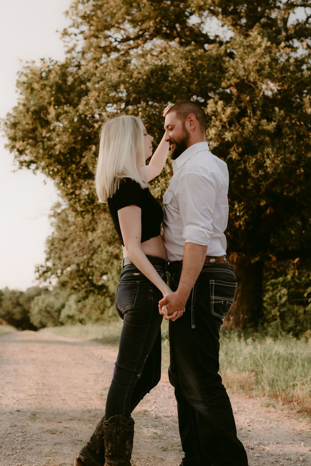 A tender moment between a couple on a rural path surrounded by lush summer foliage.