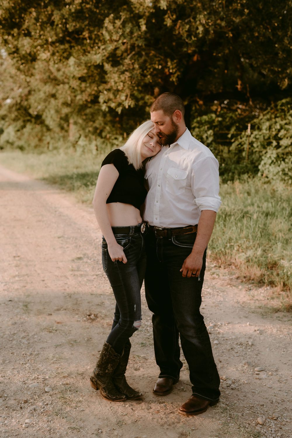 A couple shares an intimate moment while standing together on a country path at sunset.