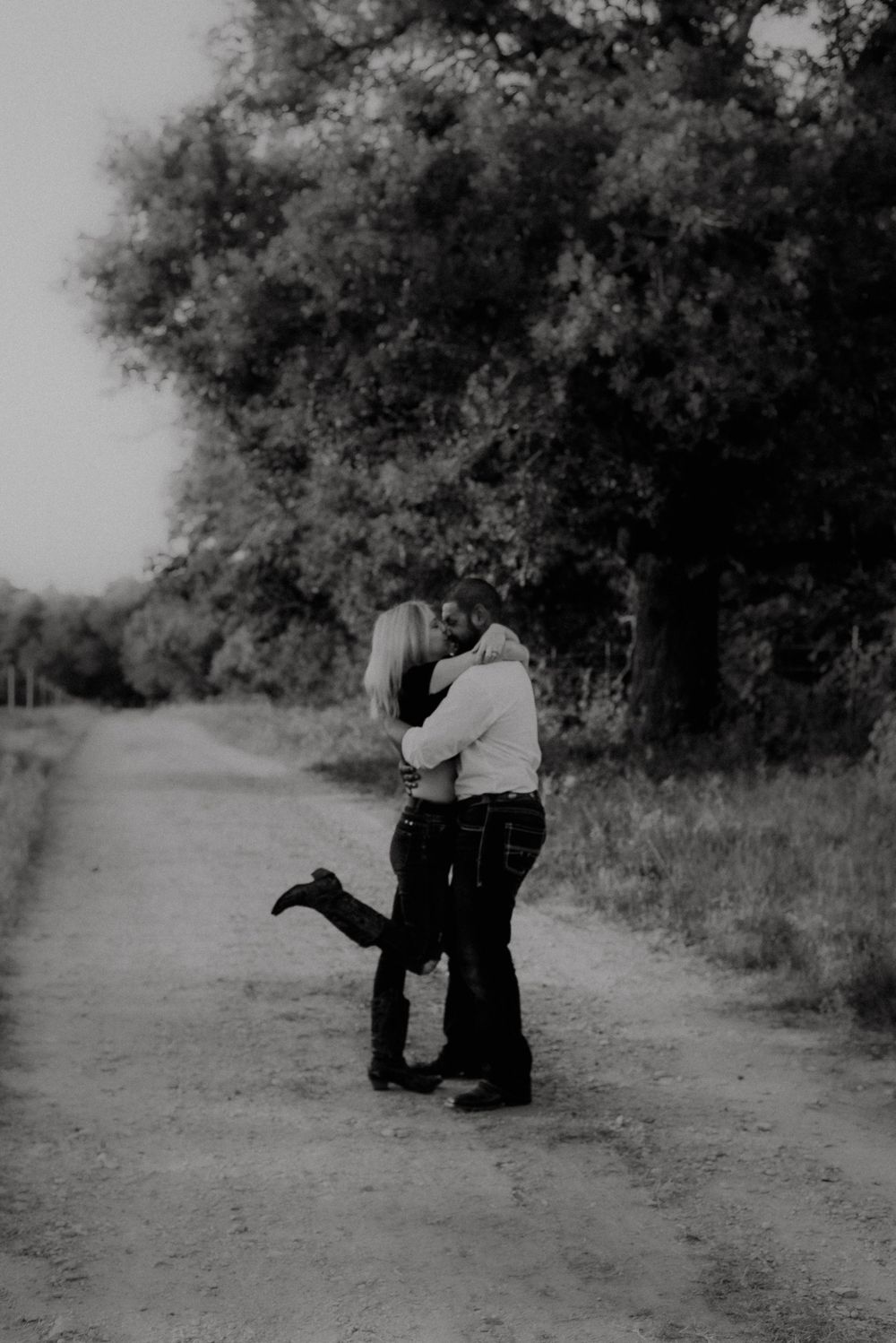 A black and white photo captures a romantic embrace on a secluded country path.