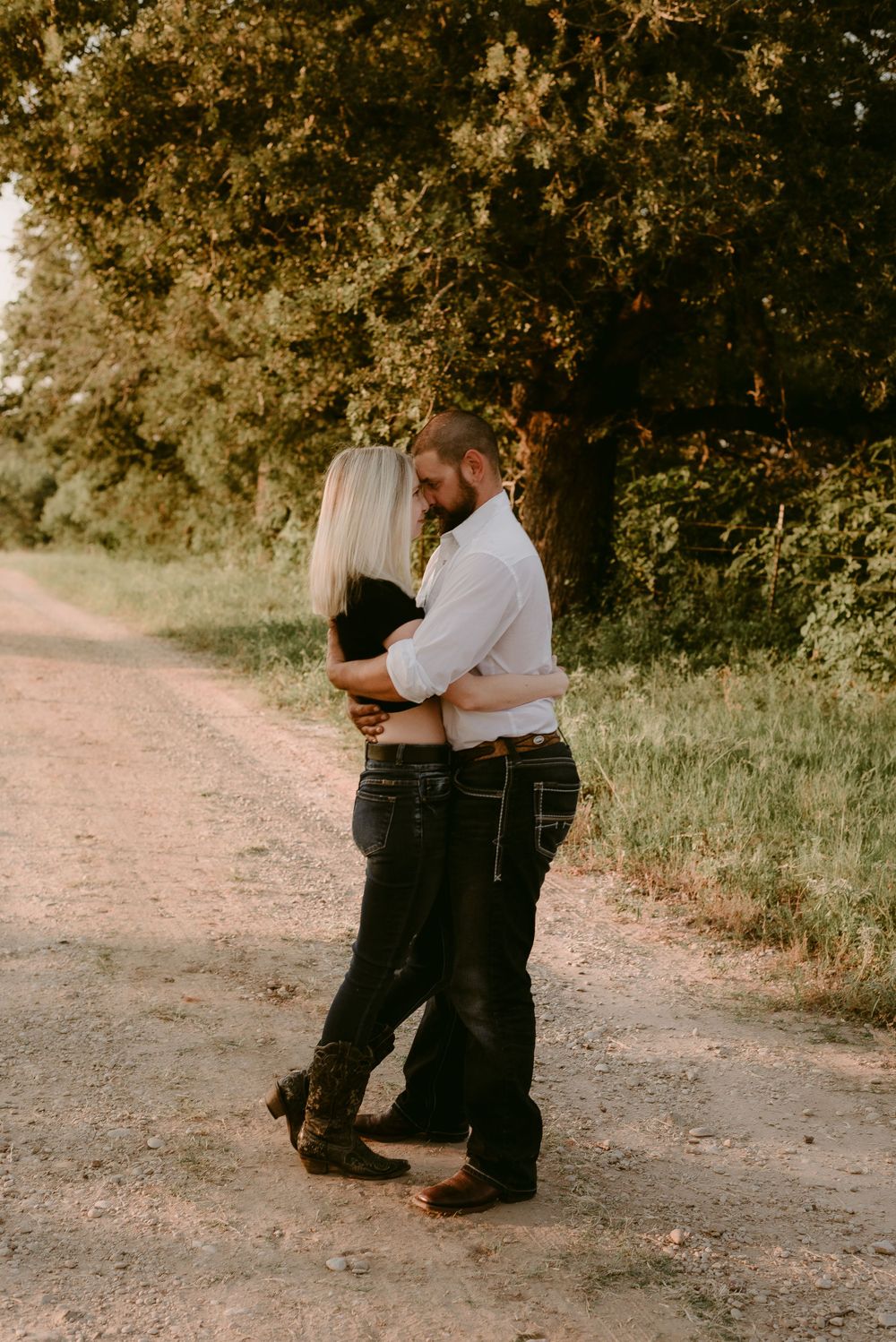 A couple slow dances together on a dirt path during sunset with trees in the background.