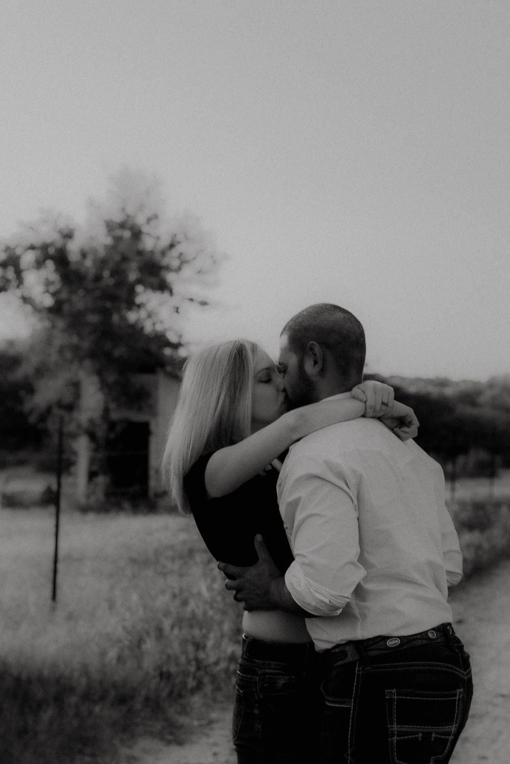 A black and white portrait of a couple sharing an intimate moment on a country path.