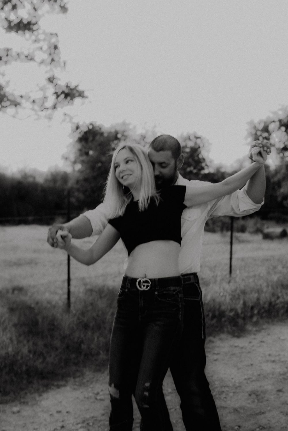 A black and white photo of a couple sharing a playful dance moment outdoors.