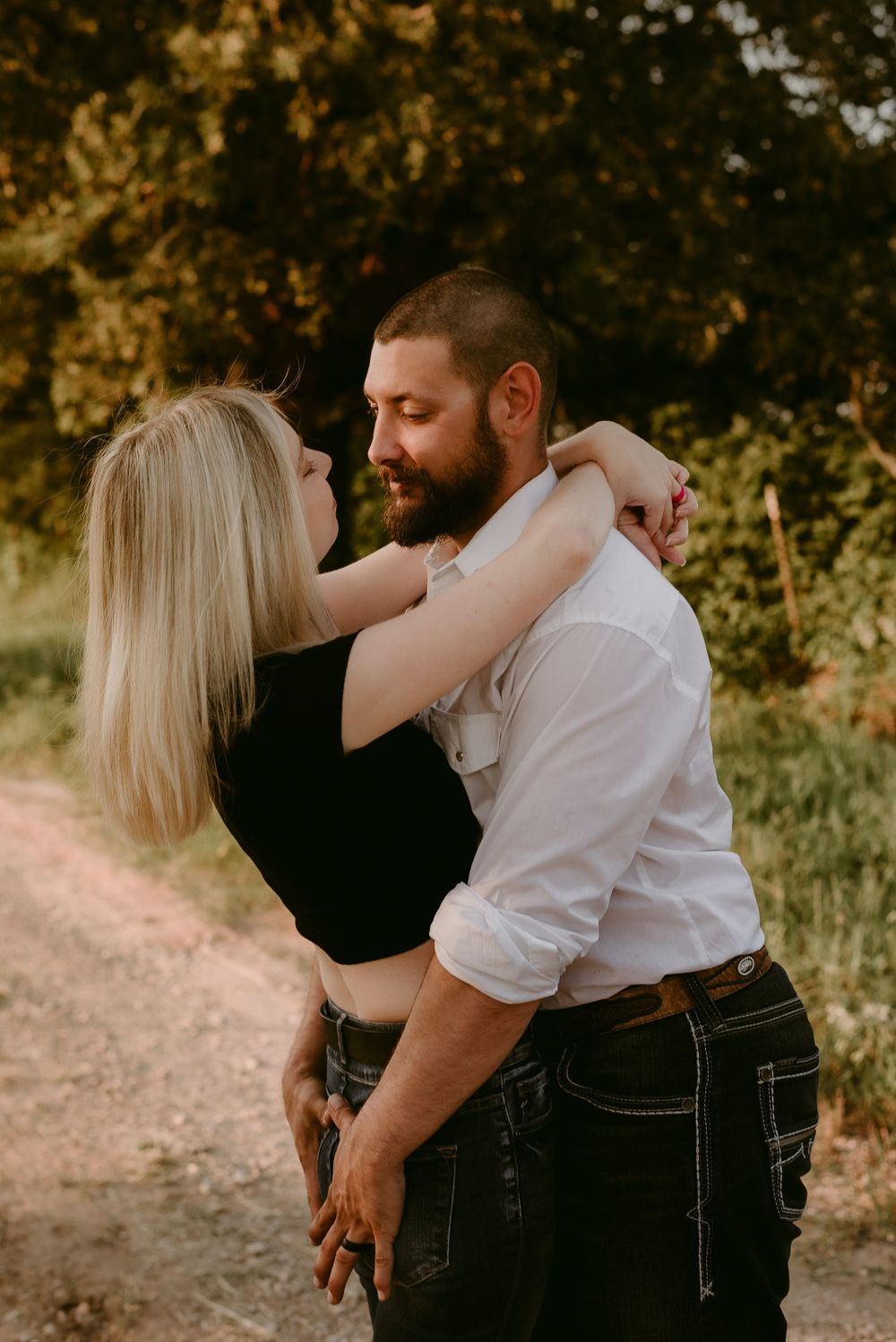 A romantic countryside photo session with a couple embracing on a dirt path during golden hour.
