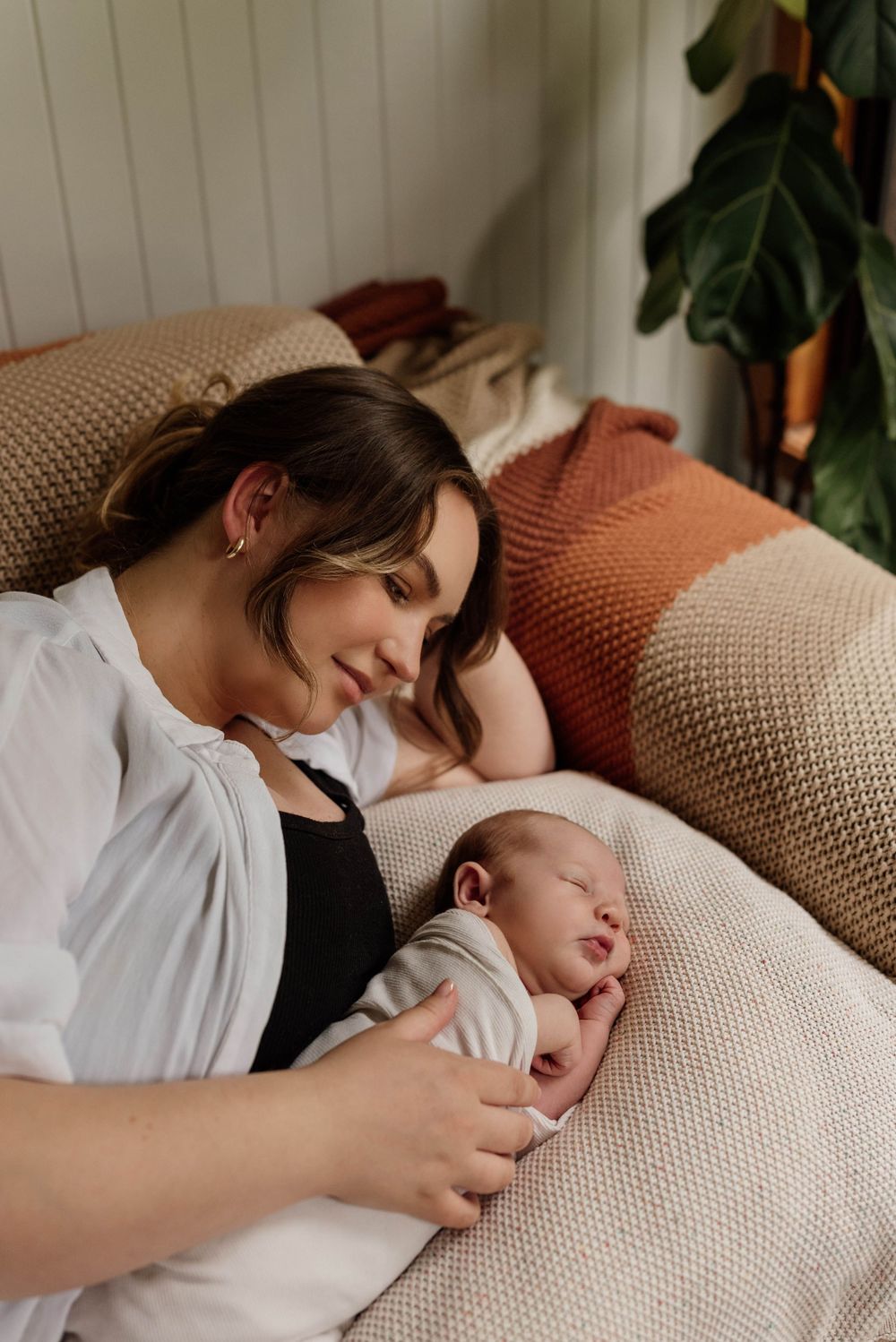 New mother in white shirt gazing lovingly at sleeping newborn baby during in-home lifestyle session.