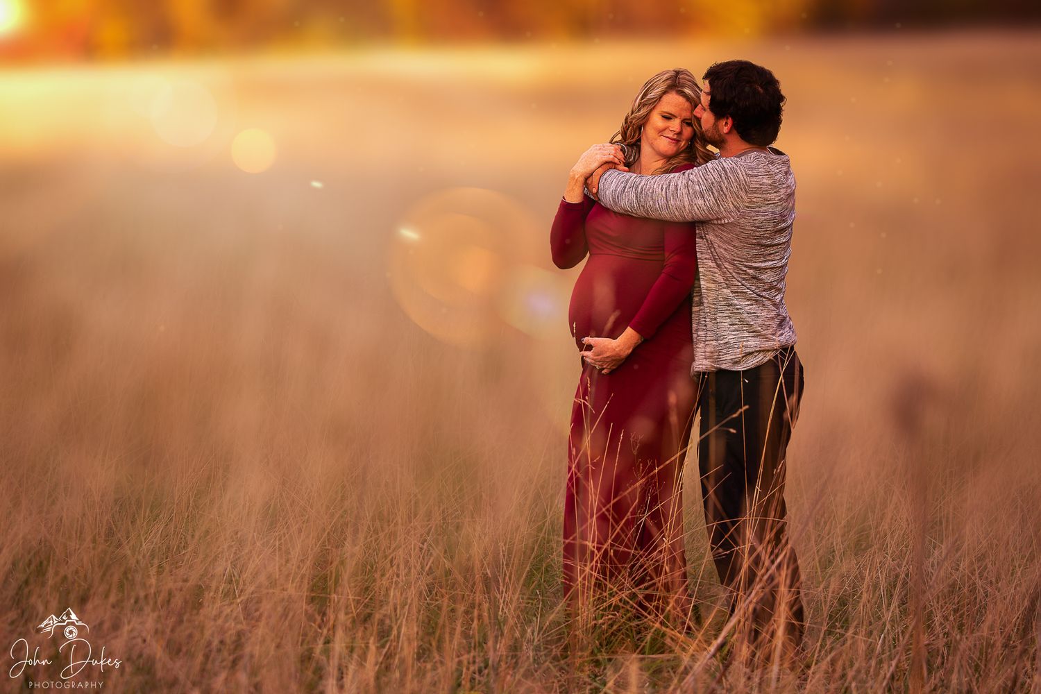 Couple embraces in a golden sunset field during photo session.