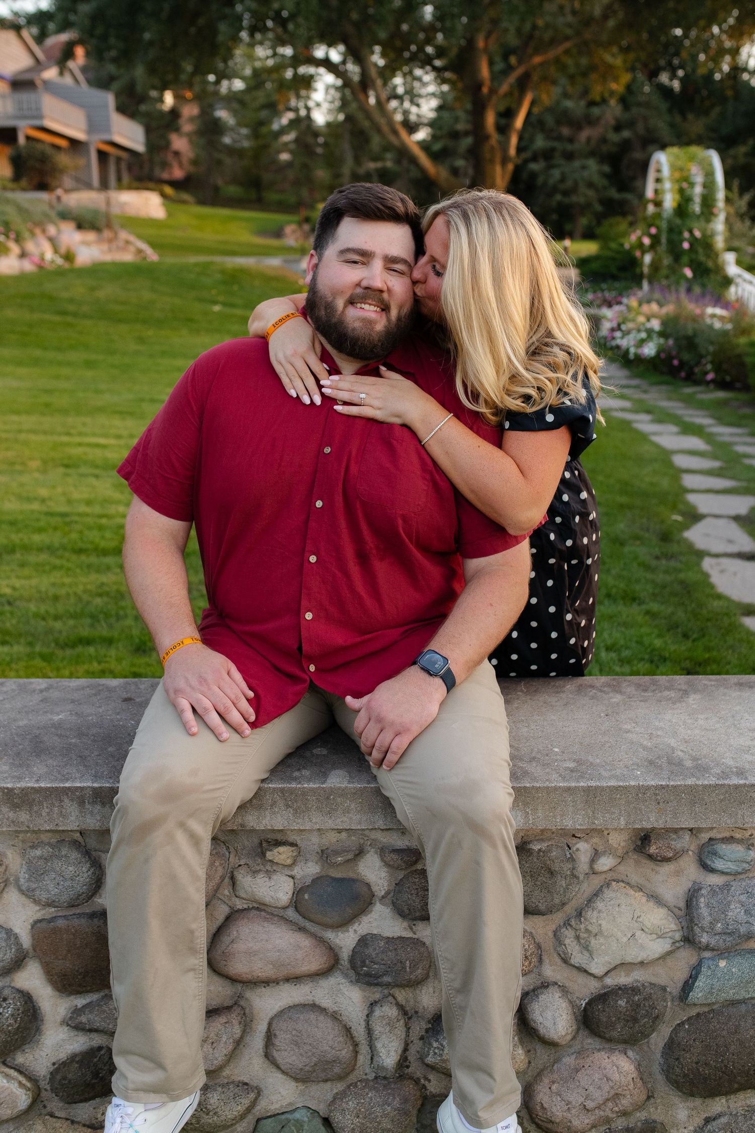 Couple sharing intimate moment while sitting on stone wall in garden setting. Couples photo session. Engagement photo session. Lake Geneva W