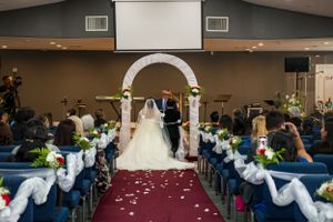 Wedding ceremony setup with white arch and red carpet aisle in church with blue pews.