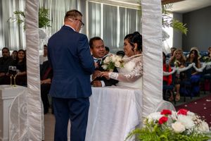 Wedding reception scene with decorated arch and guests gathering around white-covered tables.