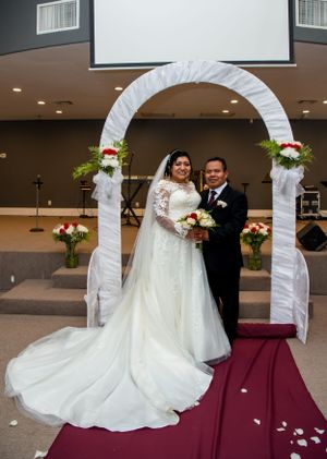 Wedding ceremony setup with white arch and rose petals on burgundy carpet indoors.