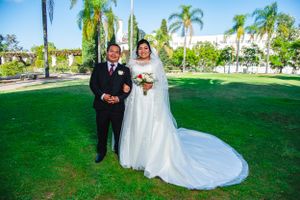 Wedding couple poses on green lawn with palm trees in tropical outdoor setting.