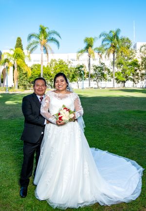 Wedding couple poses on grass lawn with palm trees and blue sky in background.