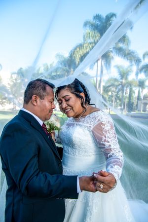 Romantic wedding portrait with flowing veil against palm trees.