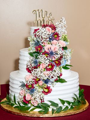 White wedding cake decorated with pink and red flowers and a gold 'Mr & Mrs' topper.