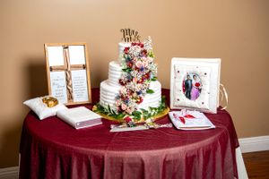 Elegant three-tier white wedding cake with cascading floral decorations on burgundy tablecloth.