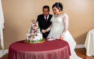 Wedding couple cutting into an elegant white tiered cake decorated with fresh flowers.