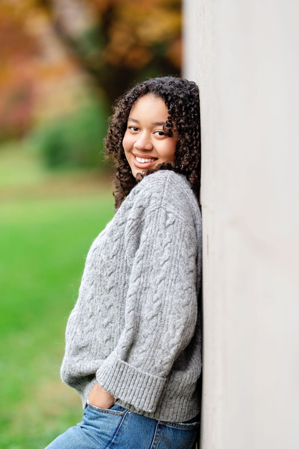 Senior photo of a girl leaning on a gray wall looking over her shoulder in the fall taken by Milwaukee senior photographer Rachel Dickman.