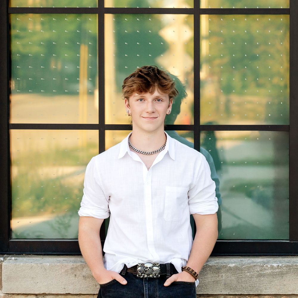 Senior photo of a boy leaning in front of a window with a geometric design behind him taken by Milwaukee senior photographer Rachel Dickman.