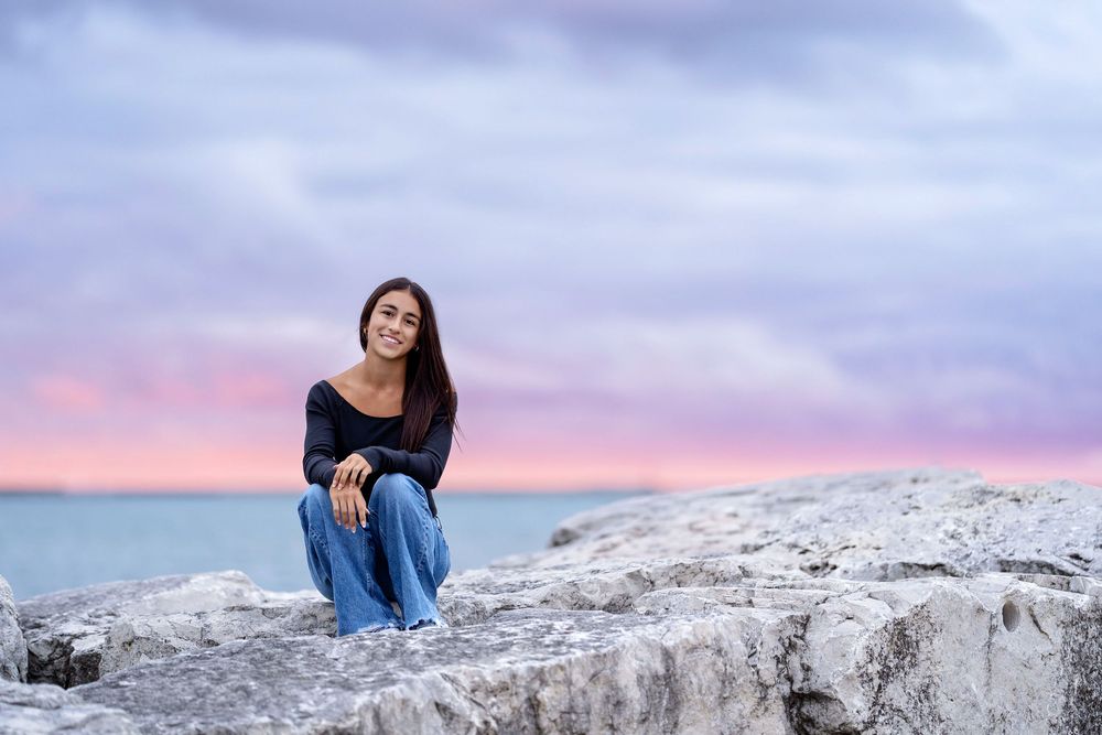 Senior photo of a girls sitting on rocks at sunset with water behind her taken by Milwaukee senior photographer Rachel Dickman.