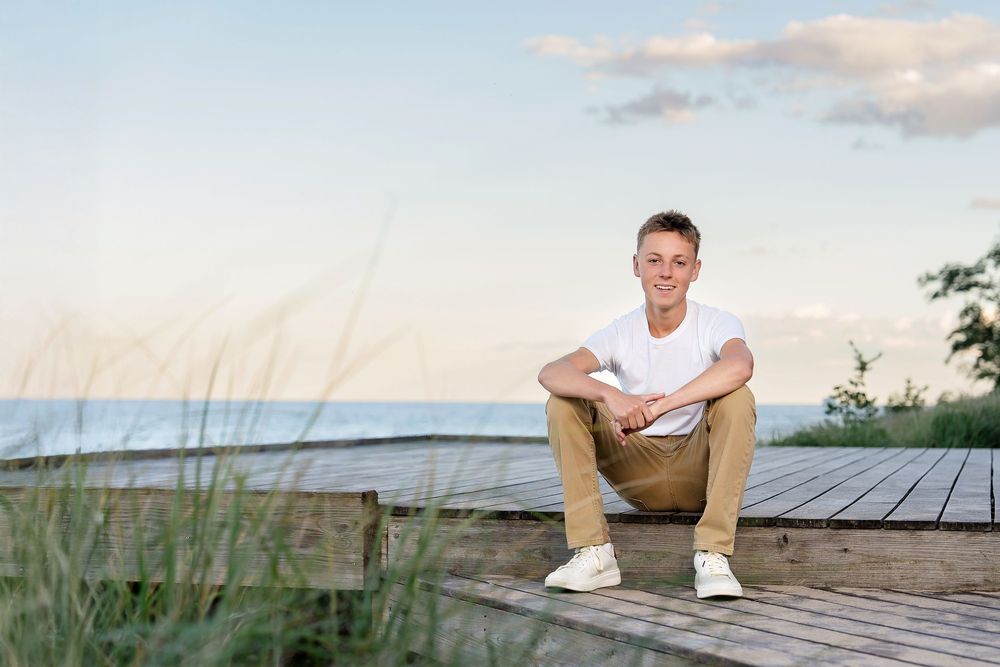 Senior photo of a boy at sunset taken on a boardwalk with water behind him taken by Milwaukee senior photographer Rachel Dickman.