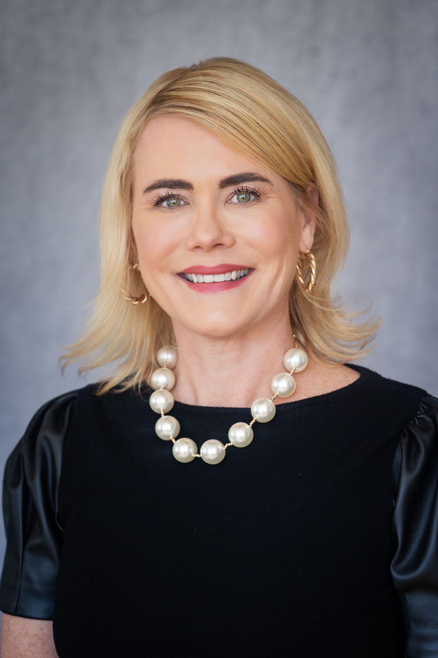 Business woman in black top and pearls smiling against blue backdrop - professional headshot photo by Milwaukee photographer Rachel Dickman.