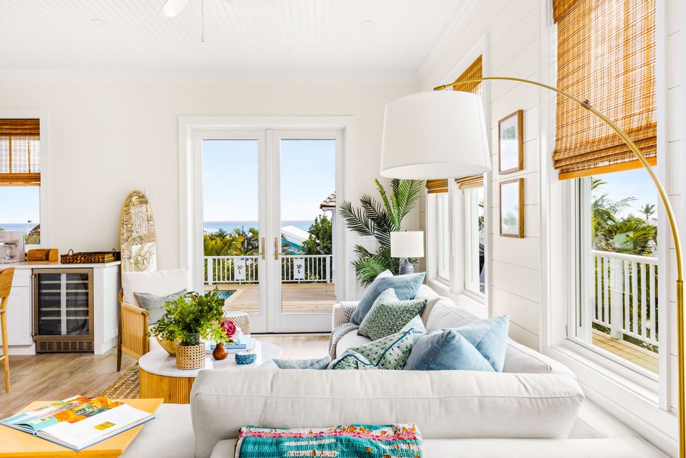 Bright white coastal living room with blue accents, bamboo shades, and ocean view balcony.
