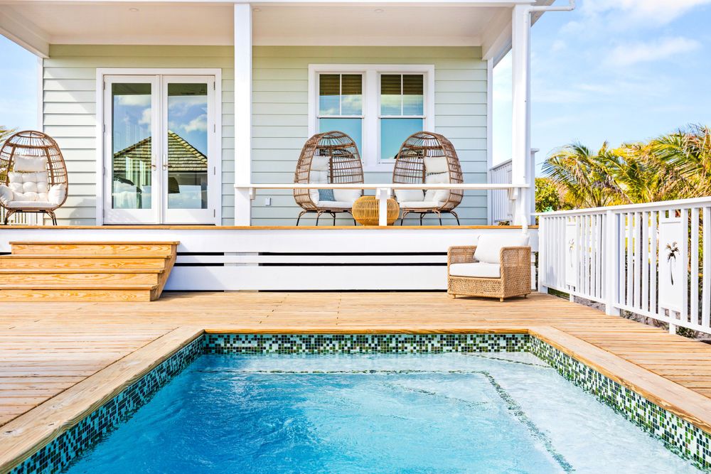 Charming beach house with private pool, wooden deck, wicker chairs, and lush tropical surroundings.