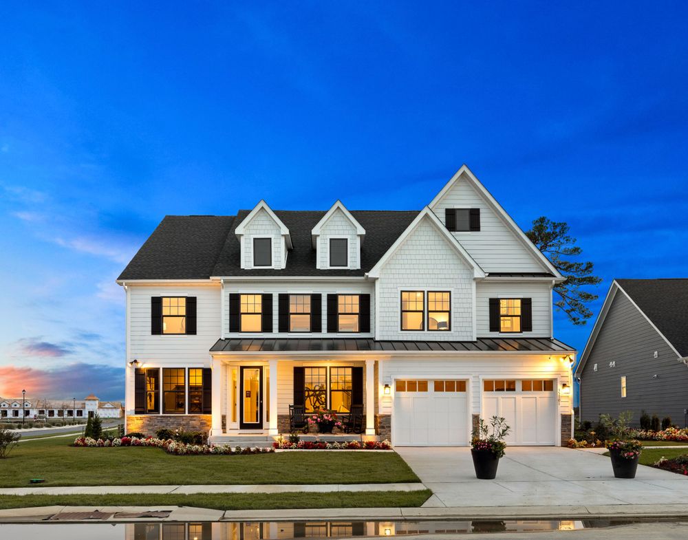 Beautiful white two-story craftsman home with black shutters, covered porch, and two-car garage at twilight.