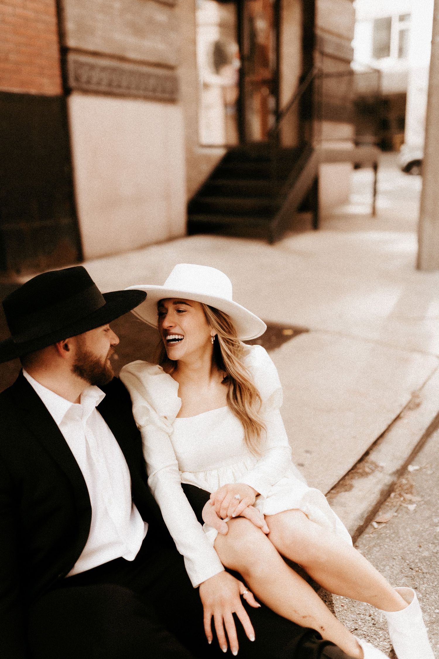 Romantic sepia-toned portrait on city steps featuring vintage-inspired fashion.