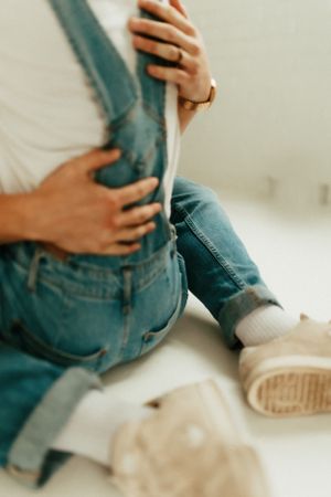 Close-up detail shot of hands and denim overalls against a light background.