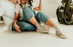 A casual intimate moment showing denim overalls and white sneakers on a light floor.