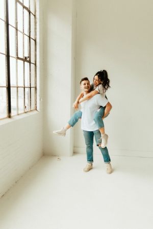 Playful piggyback ride scene in a bright white minimalist room with large windows.