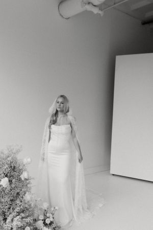 Black and white portrait of bride in sleek gown with dramatic veil and flowers.