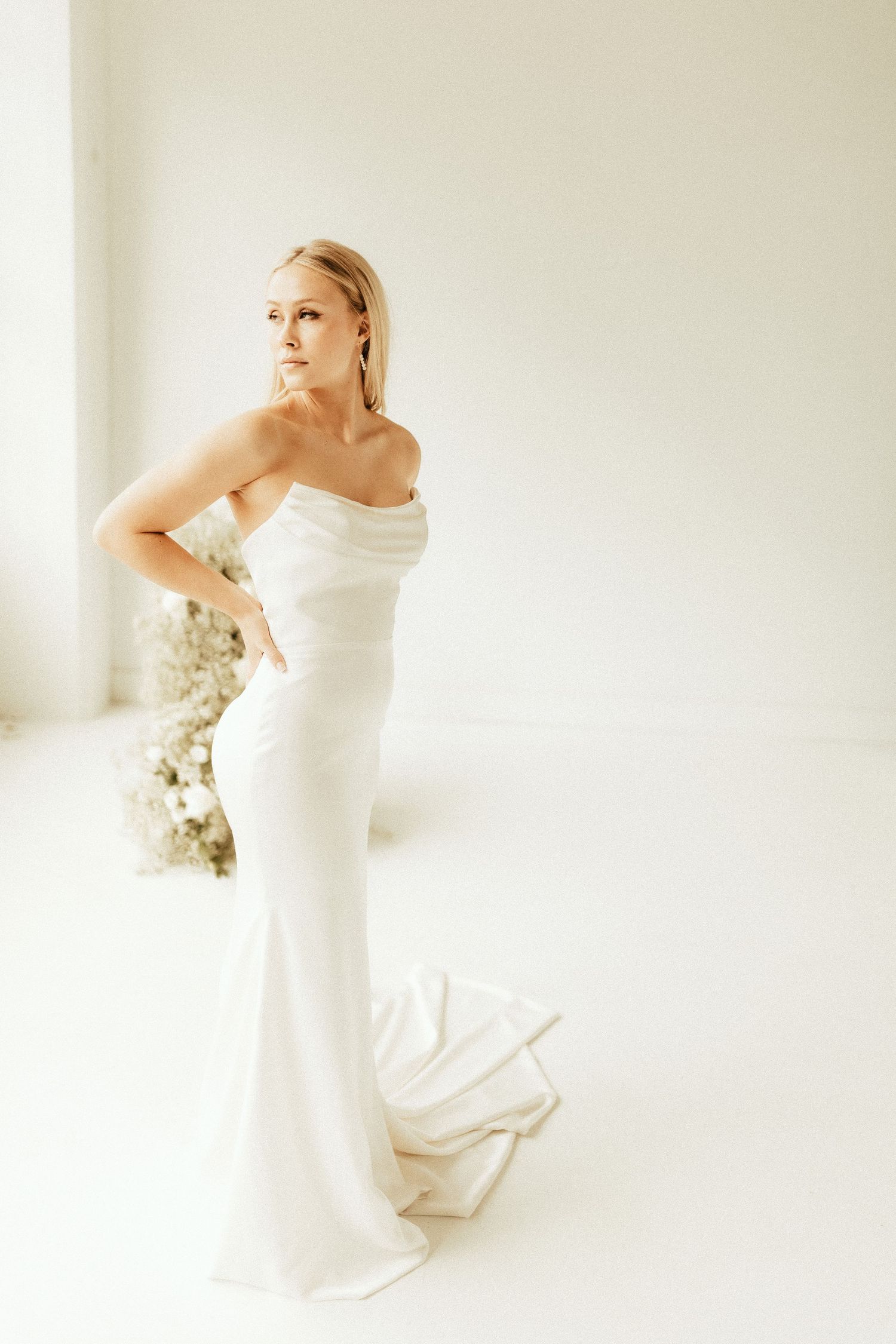 Elegant bride in fitted strapless wedding gown poses against white studio backdrop.