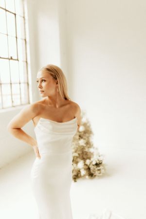 Elegant strapless white gown in a minimalist indoor setting with a decorative tree in soft focus.