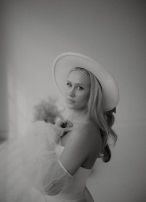 Black and white portrait showcasing dramatic bridal look with wide-brim hat and tulle sleeves.