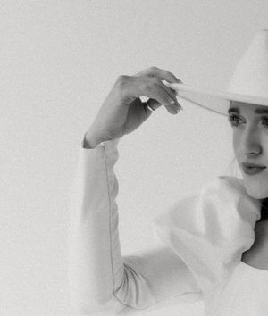 Artistic black and white portrait showing a hand adjusting a white hat brim.