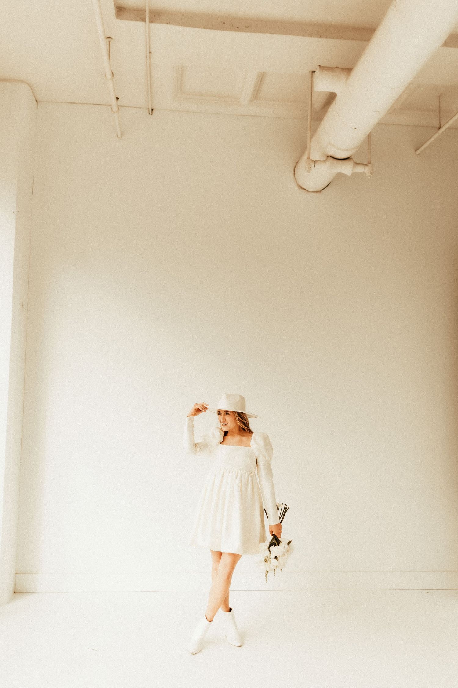 Whimsical full-length shot of white dress and boots in minimalist white studio space.