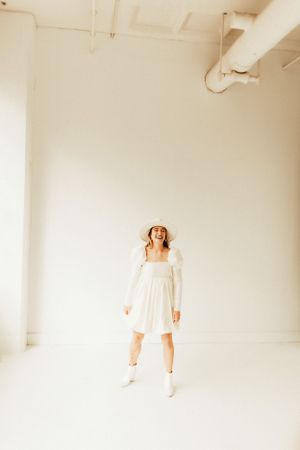 Dynamic full-body studio shot featuring short white dress and boots against industrial ceiling.