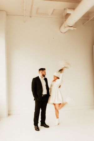 Stylish couple poses in a white studio, with her in a white dress and him in a black suit.