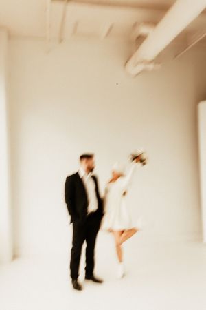 Artistic motion blur of couple in formal wear against white studio backdrop.