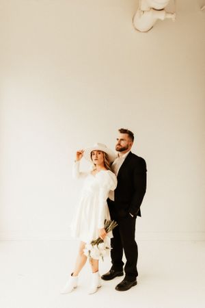 A couple in vintage-inspired attire poses in a minimalist white studio setting.