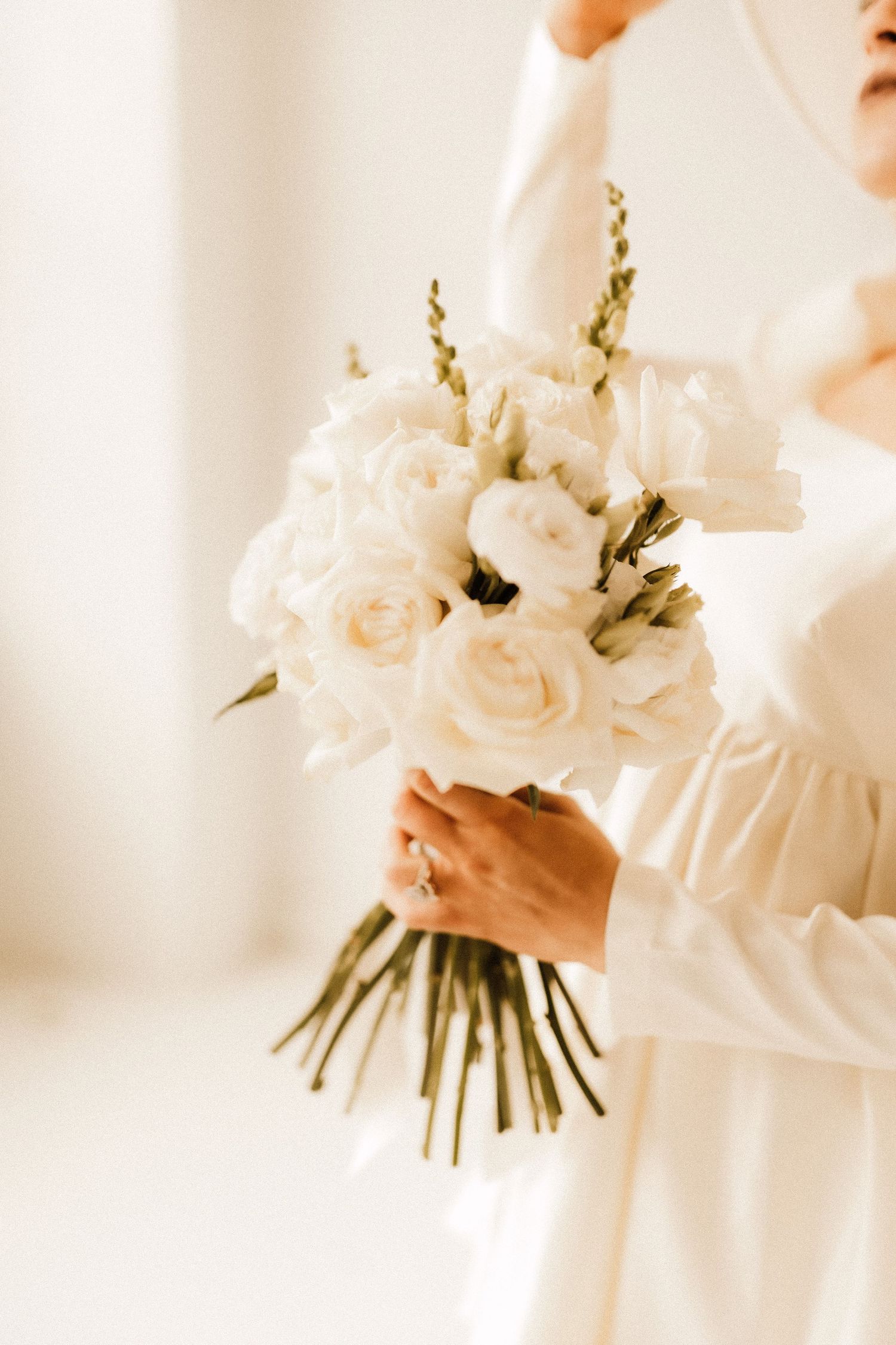 Beautiful white rose and greenery bouquet held by hands in a white dress.