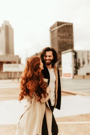 Romantic urban rooftop photo of a couple in contrasting outfits against city buildings.