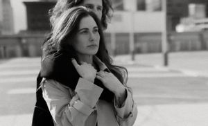 Black and white portrait of someone in a light coat against an urban setting.