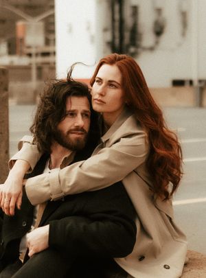 A romantic couple embraces on a city street, the woman wearing a beige coat and having long red hair.